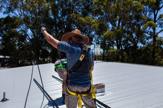 Electrician apprentice untangling cables on roof for solar panel installation job