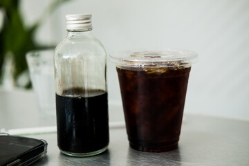 A glass of ice black coffee and a bottle filled with more of the same dark, rich beverage.