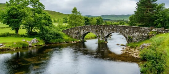 Picturesque arched stone bridge spanning a serene river in lush green scottish highlands