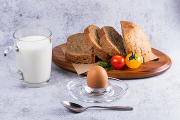 Delicious breakfast with sliced bread, fresh tomatoes, a boiled egg, and milk served on a wooden plate