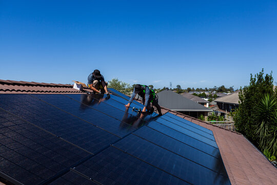 Team of workmen laying all Black bifacial solar panels on roof