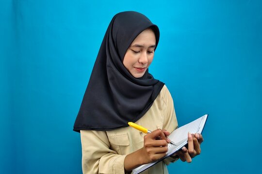 Young Muslim woman wearing hijab writing in notebook at study desk. Symbol of education, goal setting, journaling, and focus on personal growth. - Powered by Adobe