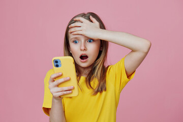 A shocked young girl in a bright yellow shirt reacts with disbelief while looking at her phone...
