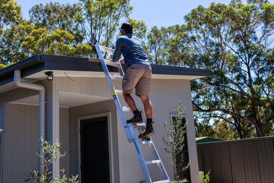 Electrician tradie man climbing up ladder to roof for solar panel installation job