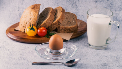 Delicious breakfast with sliced bread, fresh tomatoes, a boiled egg, and milk served on a wooden plate