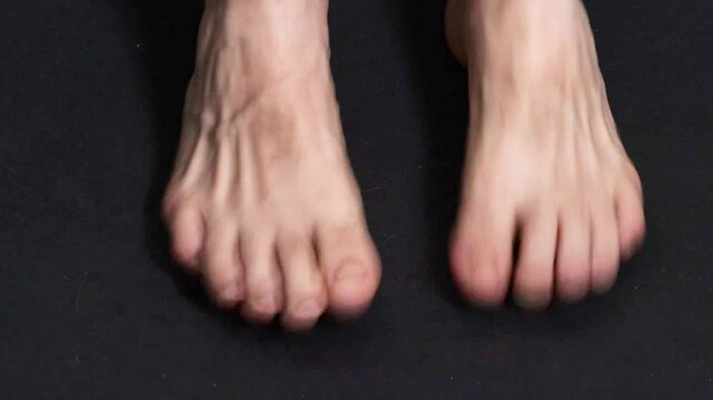 Close-up of barefoot man's feet moving on black background, moving toes, stomping. High quality FullHD footage