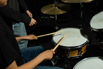 Young caucasian woman teaches a boy to play the drums in the studio on a black background. Music school student