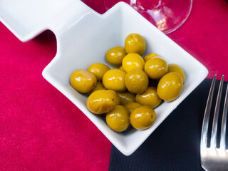 Cup of pickled olives with a stone and a wine glass on a crimson background...