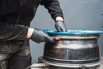 Mechanic removing protective film from alloy wheel rim in auto repair shop
