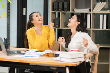 Two Asian businesswomen raise their hands in joy in their company.