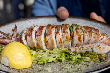 Traditional greek cuisine, grilled squid with piece of lemon and green salad, dish on a plate in a restaurant, Greece