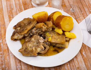 Traditional Spanish braised pettitoes, spicy pig feet cooked with sauce served with vegetable garnish of baked potatoes in skin