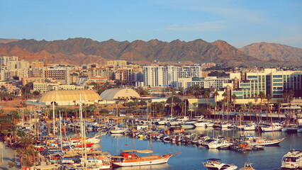 Eilat Marina Coastal Cityscape Mountain Background Aerial View Warm Color. Sunny Israeli Seaside Port Modern Buildings Boats Reflected In Water