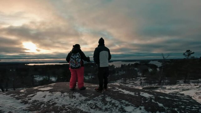 Back-shot of two hikers stand at the top of the Huckleberry Rock lookout in Muskoka, Canada at dusk