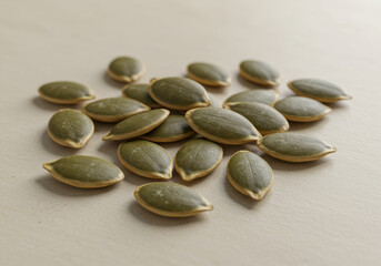 A collection of fresh, raw pumpkin seeds presented on a light, neutral background.
