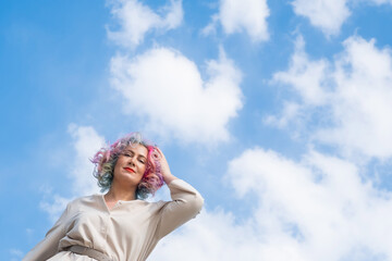 A woman with colored hair walks outdoors. Portrait of a girl against the blue sky. 