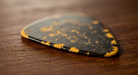Close-up Shot of a Well-worn, Black and Gold Guitar Pick Resting on a Wooden Surface