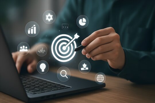 Close-up of a person's hands using a stylus on a laptop, interacting with a digital target graphic and various business icons.