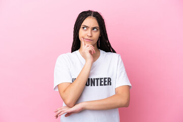 Teenager volunteer girl with braids isolated on pink background having doubts while looking up