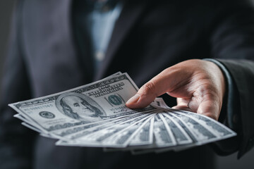A hand extends to offer a fan of hundred-dollar bills, symbolizing wealth, business transactions, and financial dealings.