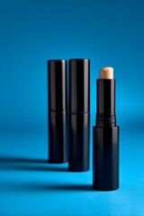 Obraz premium Three black makeup sticks against a vibrant blue background. A light beige stick is visible in the center