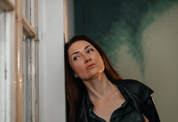 Fototapeta premium Caucasian female adult with thoughtful expression leaning against wall indoors