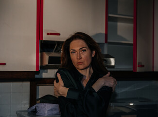 Pensive caucasian female adult posing in dimly lit kitchen interior