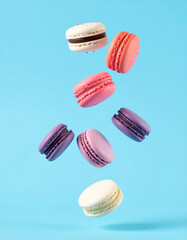 Colorful macaroon cookies falling over vivid blue background. Tasty dessert. Sweet food.