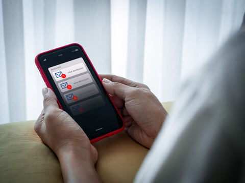 SMS spam and fake text message phishing concept. System hacked warning alert, email hack, scam malware spreading virus alert, notification on mobile phone screen in senior female hands in bedroom.