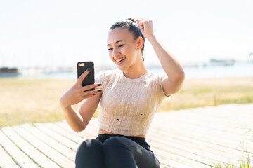 Young moroccan girl  at outdoors using mobile phone and doing victory gesture