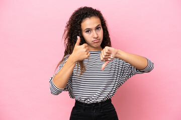 Young hispanic woman isolated on pink background making good-bad sign. Undecided between yes or not
