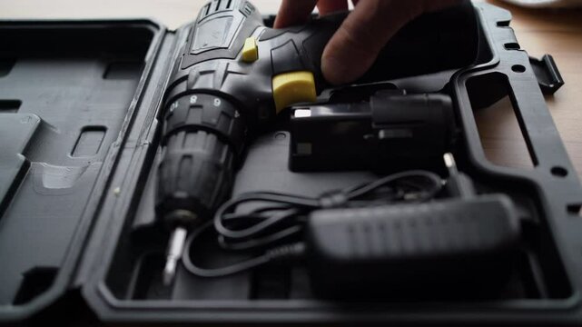 The hand of a master puts an electric drill into a box and closes the lid. Close-up.