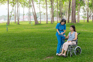 Fototapeta premium Woman doctor is taking an elderly person in wheel chair to relax in park help elderly person relax after elderly person injured his ankle and could not walk by himself.doctor takes patient wheel chair