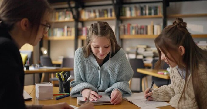 Schoolgirls engage in collaborative activities with their teacher in a vibrant library setting, surrounded by books, pens, and excitement for learning