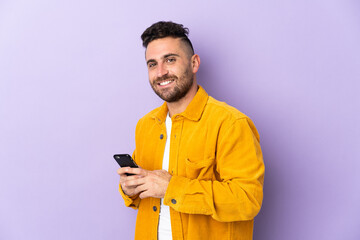 Caucasian man isolated on purple background sending a message or email with the mobile