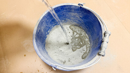 A stream of water cascades into a cobalt bucket of swirling cement, echoing Artisan's Day,...