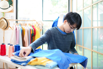 Trainee asian teenage man fashion designer  vocation and  education work on designer in the showroom,  Lifestyle Stylish tailor clothing design and cutting cloths in studio.  Education Concept