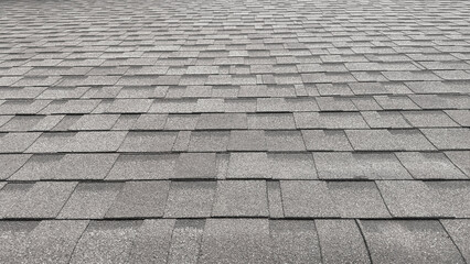 A close-up view of a gray asphalt shingle roof, showing the repeating rectangular pattern and textured surface from a low angle.