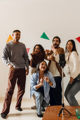 Fototapeta premium A group of young multiracial friends record a video on a smartphone while dancing and singing together in a decorated living room during a fun indoor celebration.