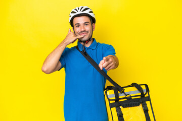Young handsome man with thermal backpack over isolated yellow background making phone gesture and pointing front