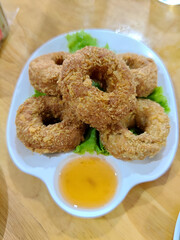 A plate of golden-brown fried shrimp cakes, shaped like rings, is served on a bed of fresh lettuce with a small bowl of sweet chili dipping sauce.