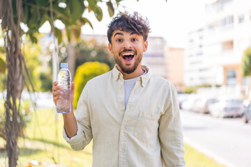 Young Arabian handsome man with a bottle of water at outdoors with surprise and shocked facial...