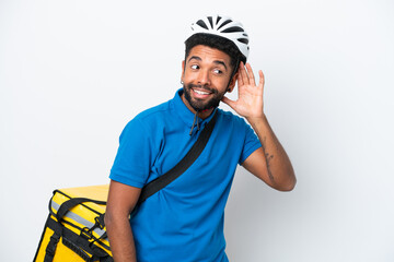 Young Brazilian man with thermal backpack isolated on white background listening to something by putting hand on the ear