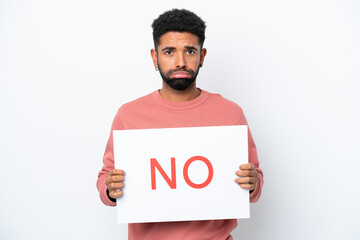 Young Brazilian man isolated on white background holding a placard with text NO with sad expression
