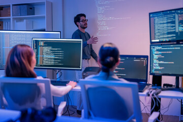 Plakat young Asian software development manager leads a late-night office discussion with his executive team, mentoring developers and analyzing source code to guide programming and project development