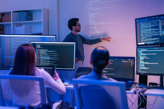 young Asian software development manager leads a late-night office discussion with his executive team, mentoring developers and analyzing source code to guide programming and project development