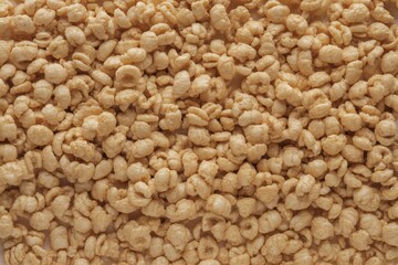 Close-up of a pile of light brown snack cereal, showcasing a crunchy texture and small, circular shapes.
