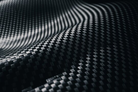 Close-up of textured black carbon fiber showcasing intricate patterns and smooth contours.