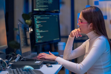 asian female programmer sits a dark tech workspace at night, fully focused on developing an online project. She writes HTML scripts and code for a modern website while contributing to automation work