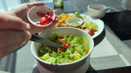 spicy food chili pepper in soup person adding sambal chili sauce to a bowl of wonton noodles, ready to eat, capturing the rich flavors and spicy culinary traditions of Indonesian street food